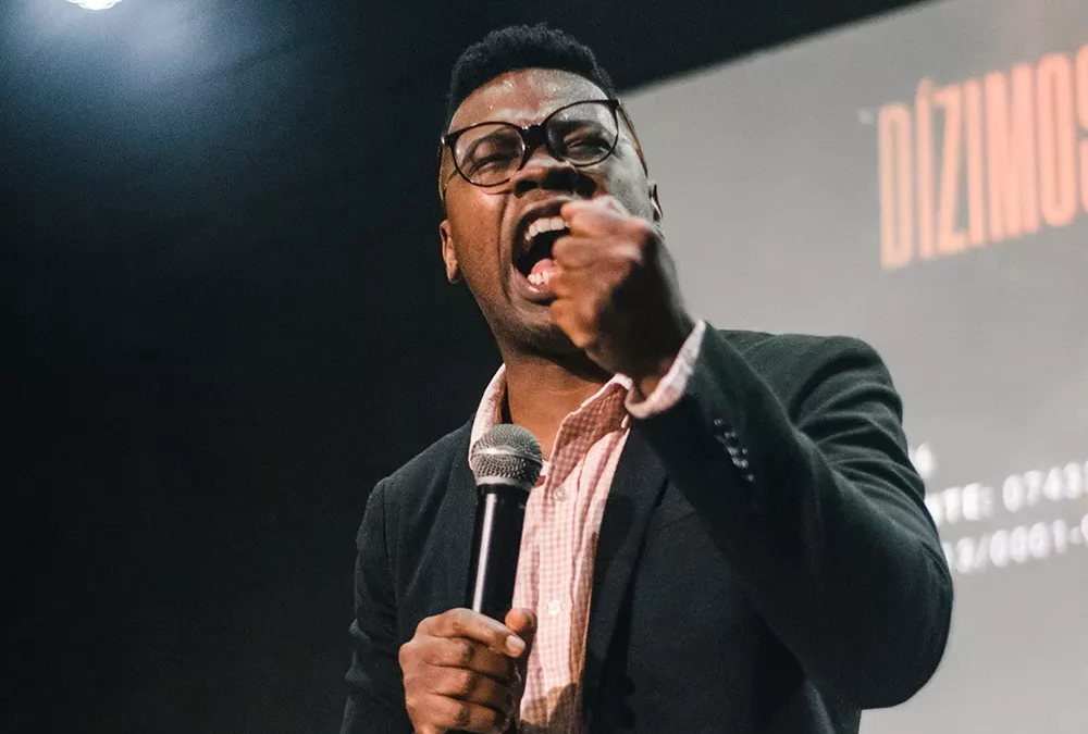 un homme avec des lunettes tient un micro à la main et fait un discours